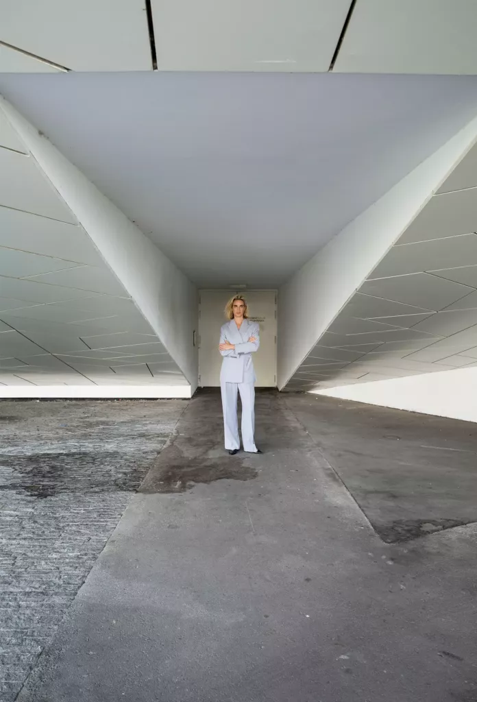 Vrouw in een lichtblauw pak staat midden in een lange, witte betonnen onderdoorgang