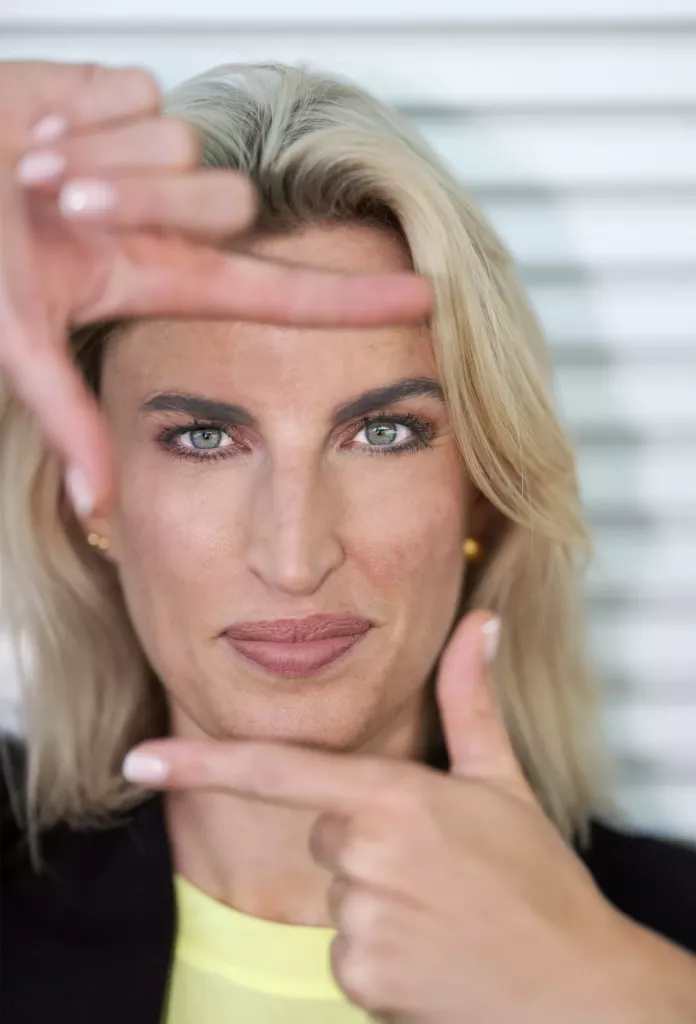Blonde vrouw maakt met haar vingers een kader rond haar gezicht en kijkt recht in de camera