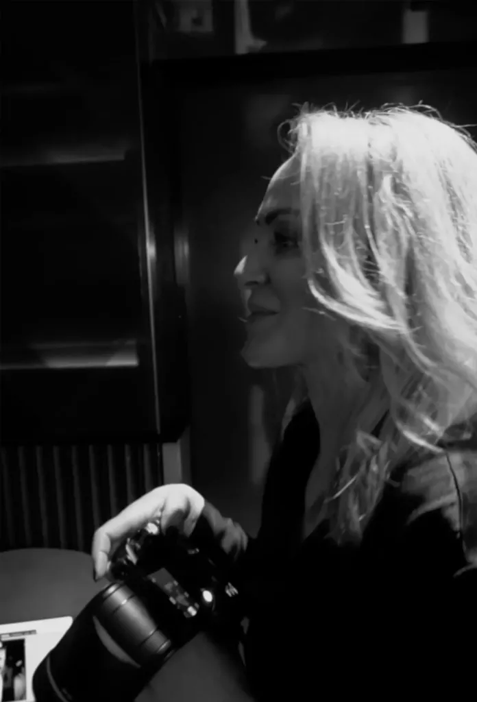 Zwart-witfoto van een vrouw met lang blond haar die met een camera in haar hand opzij kijkt