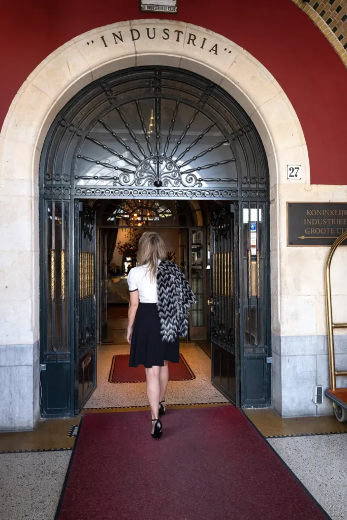 Een vrouw met een schoudertas loopt de elegante ingang van de Koninklijke Industrieële Club binnen.