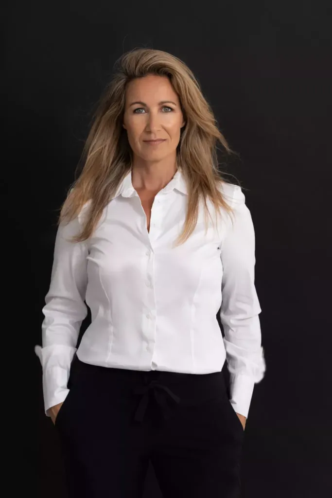 Professionele vrouw in een witte blouse met een neutrale achtergrond, straalt zelfvertrouwen en professionaliteit uit.