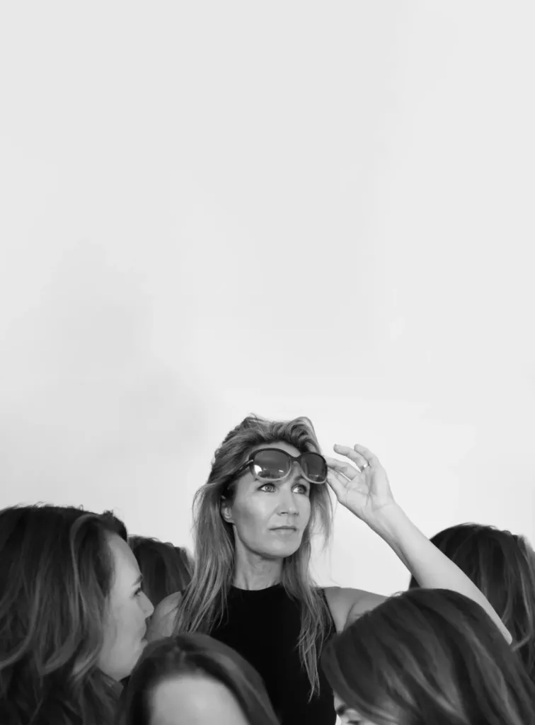 Een vrouw met een zonnebril kijkt omhoog, omringd door andere vrouwen in een zwart-wit compositie.