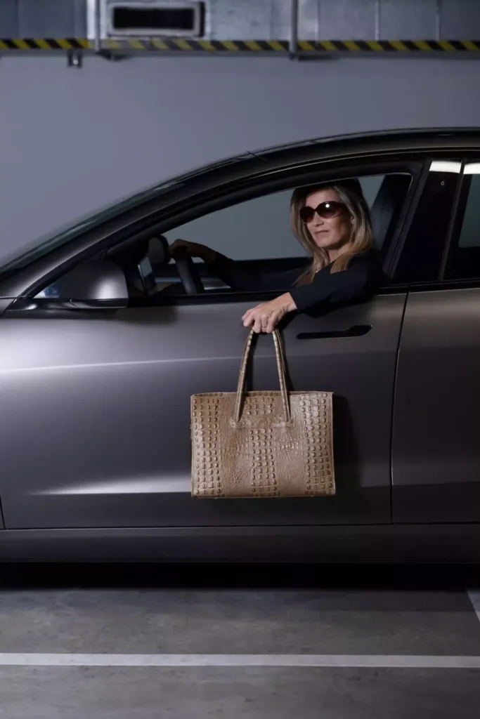 Een vrouw in een auto houdt een stijlvolle tas vast terwijl ze naar buiten kijkt.