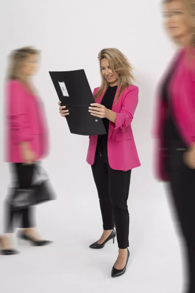 Een vrouw in een roze blazer bekijkt enthousiast een document terwijl ze omringd is door beweging.