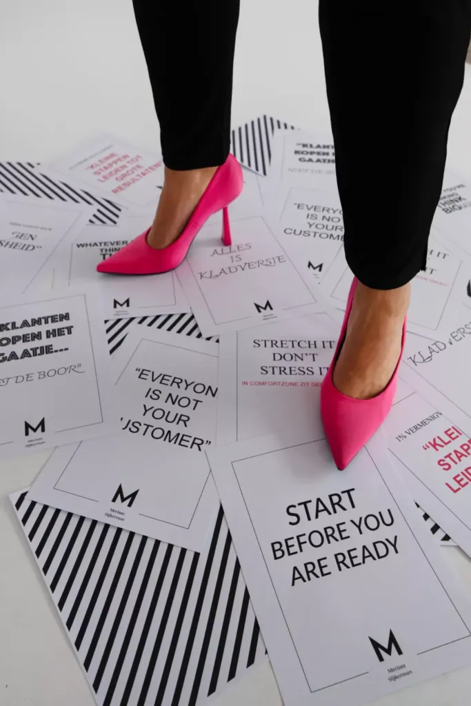 Roze hoge hakken staan op een vloer vol inspirerende en motiverende teksten op papier.