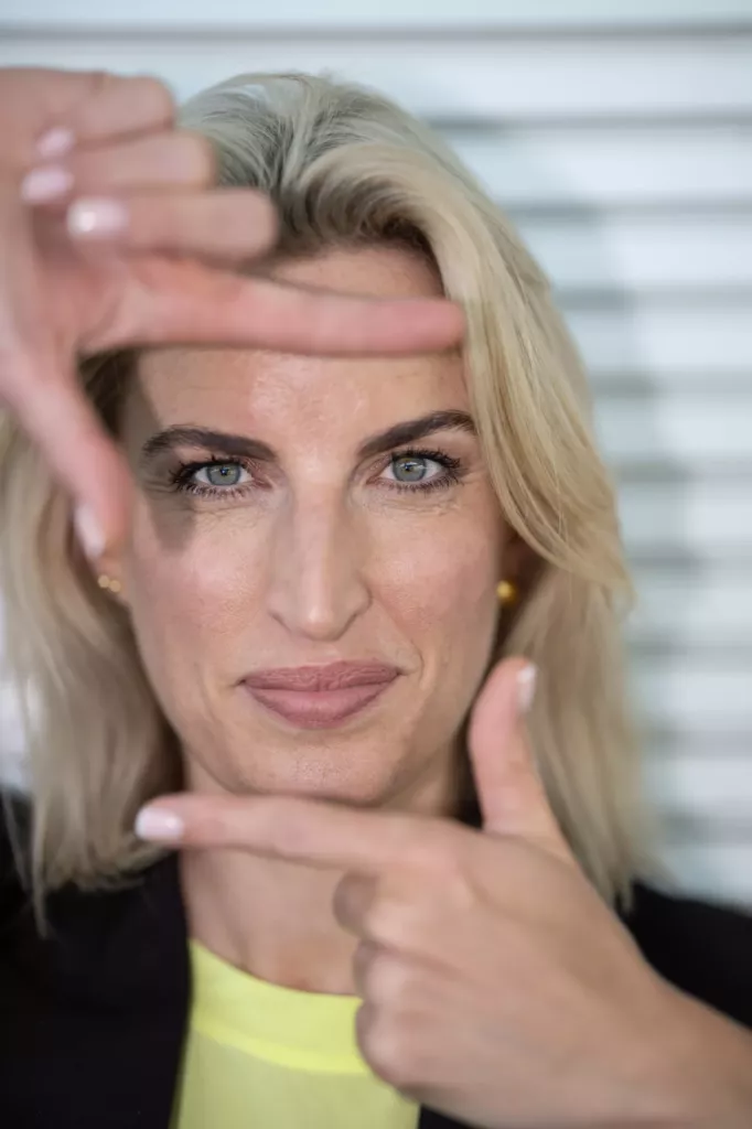 Vrouw met blond haar omlijst haar gezicht met haar handen, voor een lichte jaloezie.