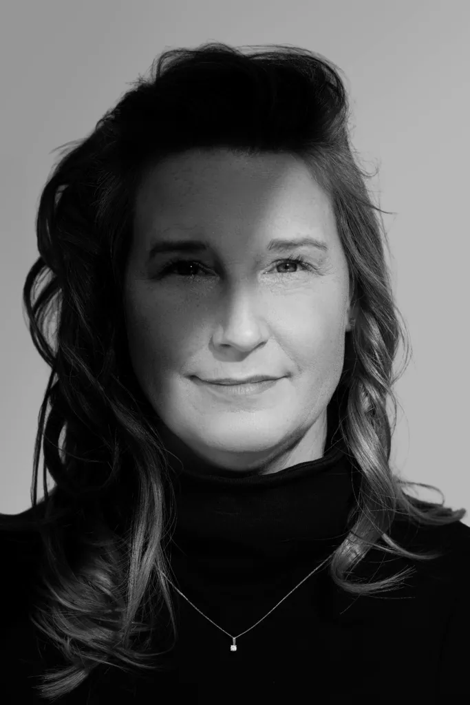 Zwart-wit close-up portret van Cynthia met golvend haar, coltrui en een fijne ketting, met een warme glimlach.