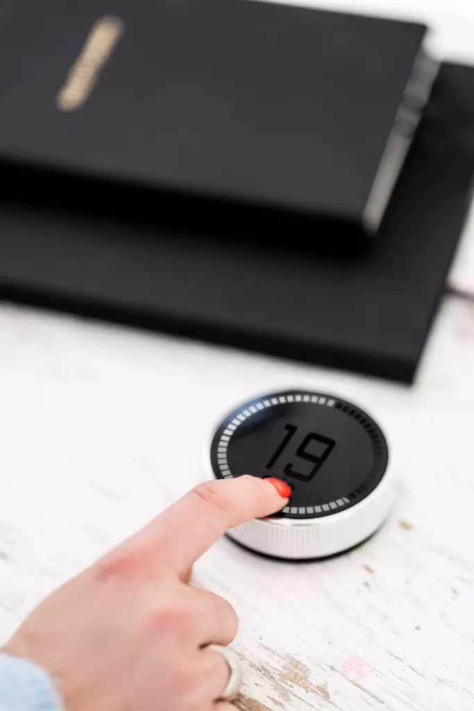 Een vinger drukt op een zwarte digitale timer die '19' aangeeft, naast zwarte notitieboekjes op een houten tafel.