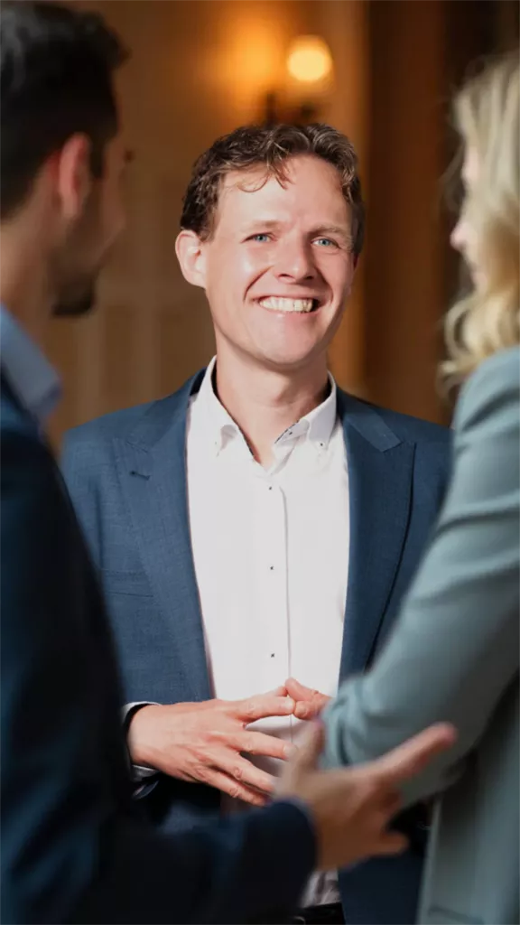 Floris Koolen in een blauw colbert, lachend in gesprek met twee mensen die half in beeld staan