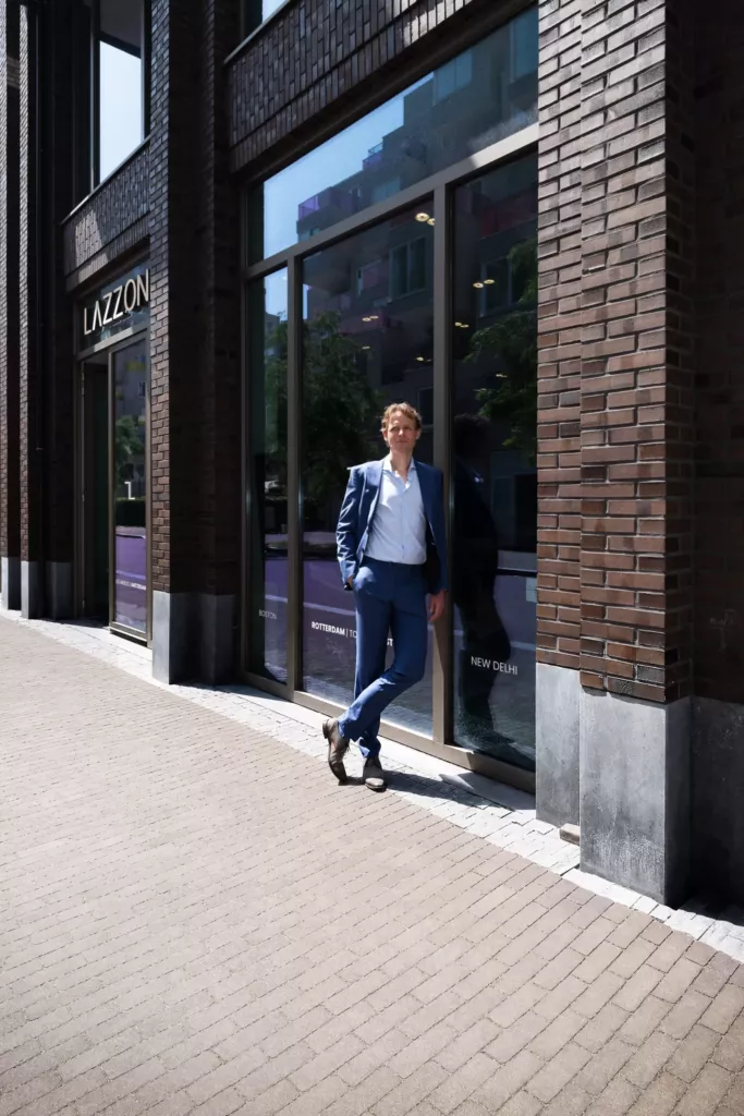 Floris Koolen in een blauw pak leunend tegen de glazen pui van een bakstenen gebouw