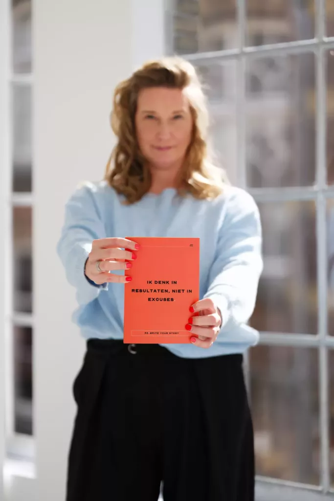 Cynthia houdt een rood boek omhoog voor een raam in een lichte ruimte.